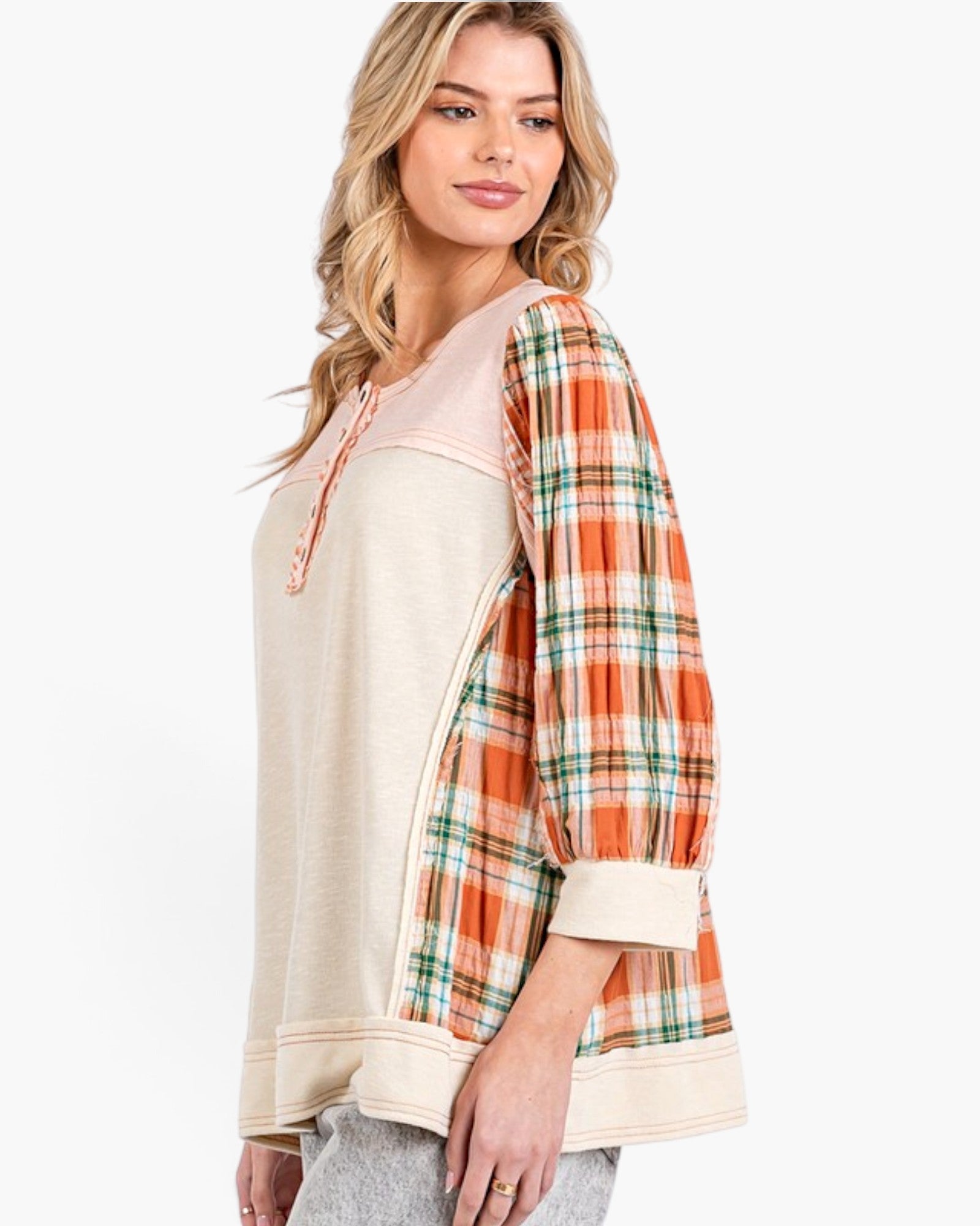 A woman wearing a cream-colored knit top with orange, green, and white plaid three-quarter sleeves, shown against a plain white studio background.