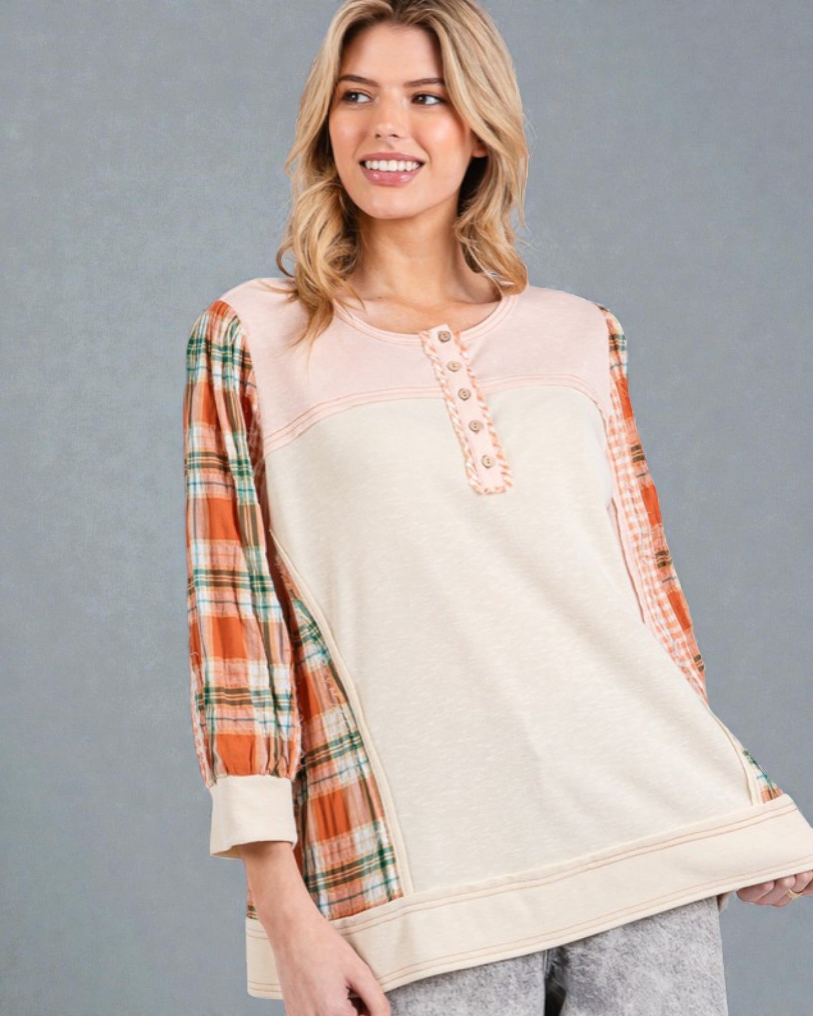 Woman wearing a cream-colored top with plaid sleeves against a gray background