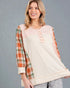Woman wearing a cream-colored top with plaid sleeves against a gray background