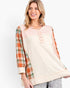 A woman modeling a color-block knit top with a cream body, a light pink henley neckline, and orange plaid sleeves, set against a plain white studio background.