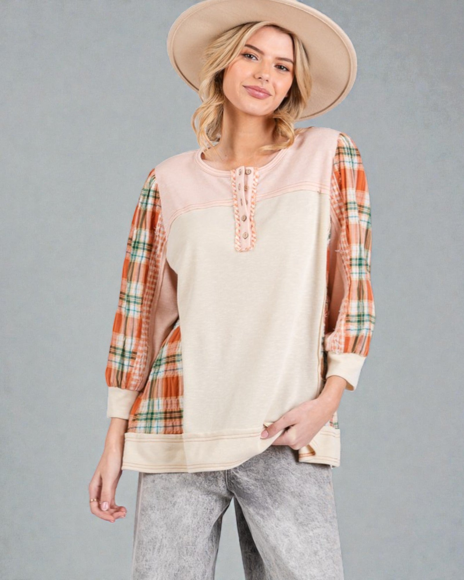 Woman wearing a plaid shirt over a beige top with a hat on a gray background