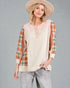 Woman wearing a plaid shirt over a beige top with a hat on a gray background
