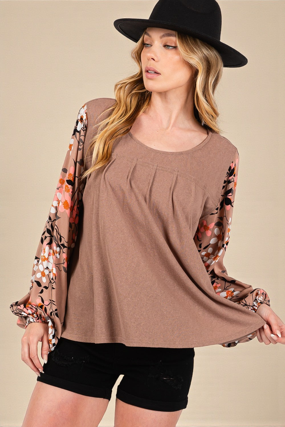 Woman wearing a brown top with floral sleeves and black shorts against a beige background