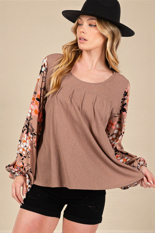 Woman wearing a brown top with floral sleeves and black shorts against a beige background