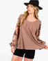 A woman wearing a brown scoop-neck top with floral printed long sleeves, paired with black shorts and a black wide-brim hat, against a plain white background.
