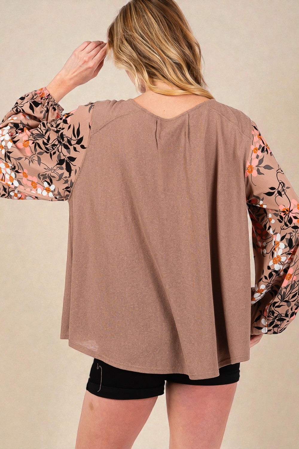 Woman wearing a brown top with floral sleeves on a beige background