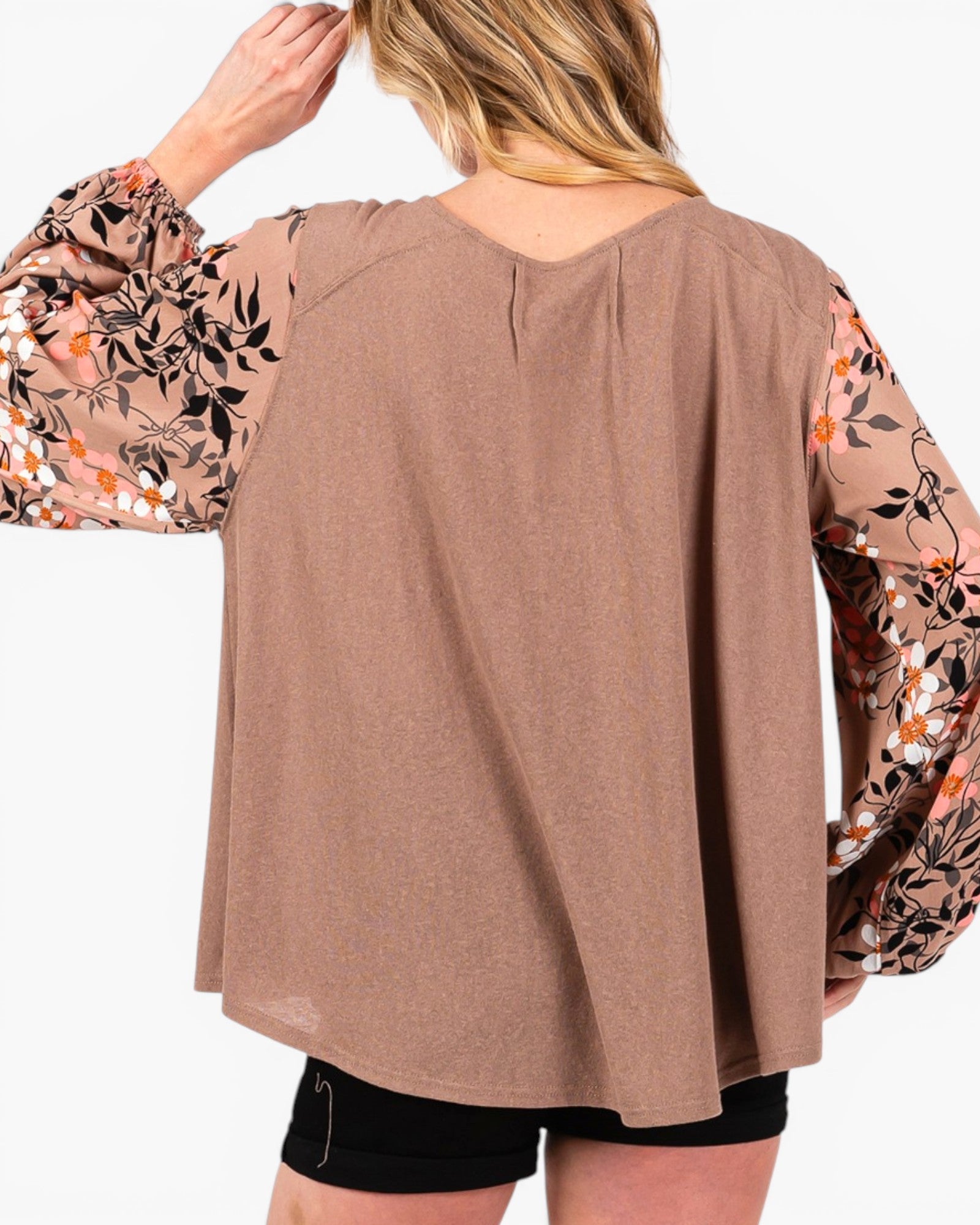A woman shown from the back wearing a loose-fit taupe brown top with long sheer floral sleeves, paired with black shorts, against a plain white background.