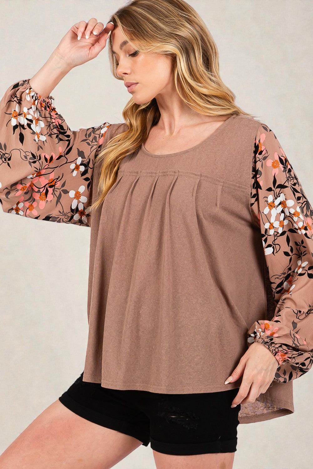 Woman wearing a brown top with floral sleeves against a plain background