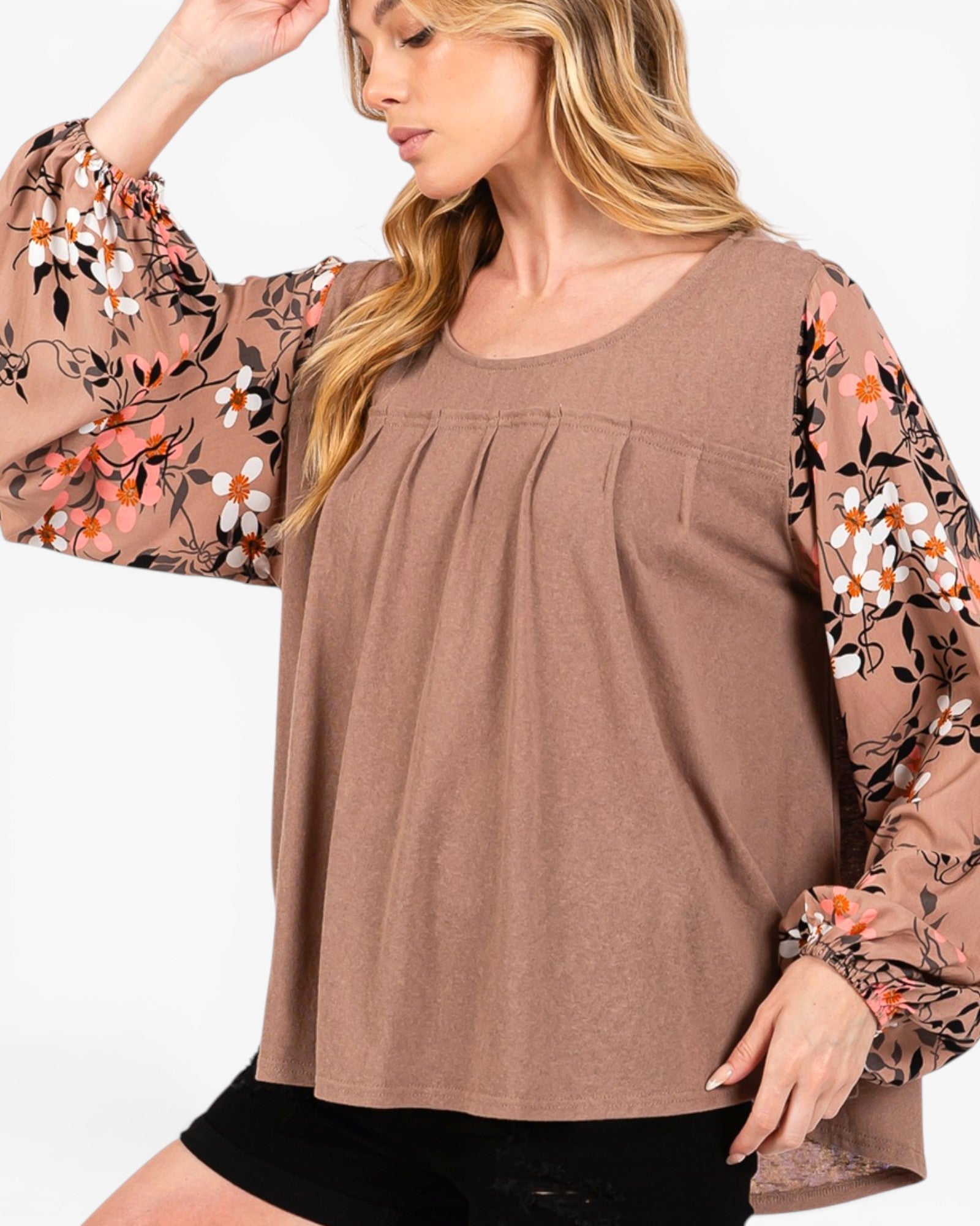 A woman wearing a brown scoop-neck blouse with long sheer floral sleeves, paired with black shorts, against a plain white background.