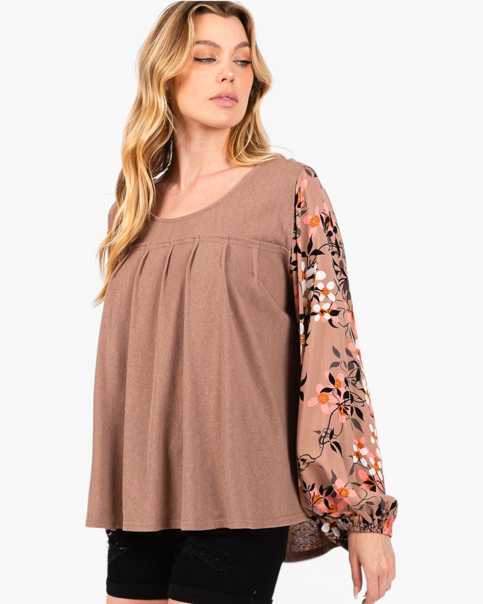 A woman wearing a brown scoop-neck top with long sleeves featuring a floral print in orange, white, and dark brown, paired with black shorts against a plain white background.