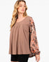 A woman wearing a brown scoop-neck top with long sleeves featuring a floral print in orange, white, and dark brown, paired with black shorts against a plain white background.