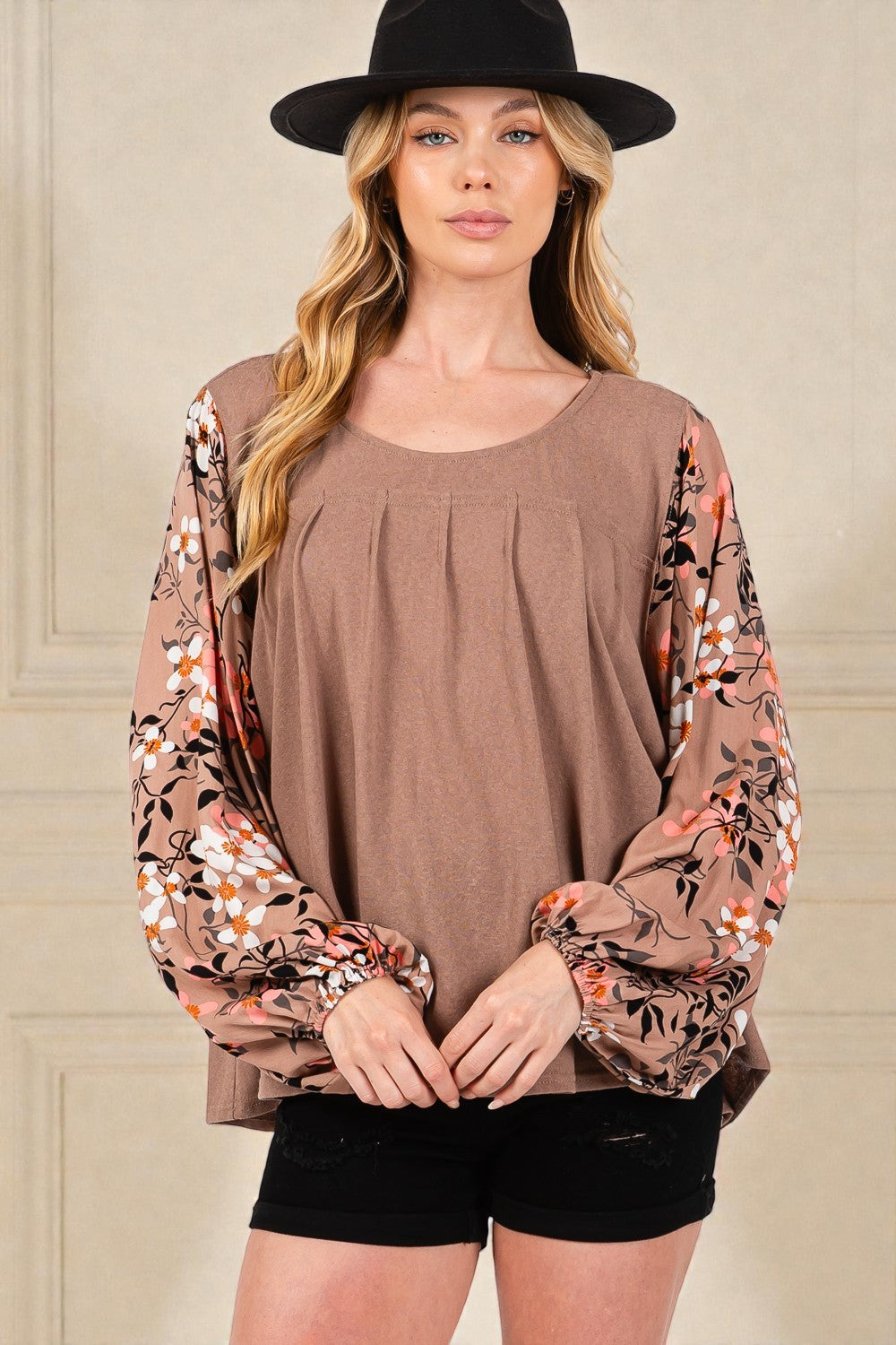 Woman wearing a brown top with floral sleeves and black shorts against a neutral background