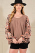 Woman wearing a brown top with floral sleeves and black shorts against a neutral background