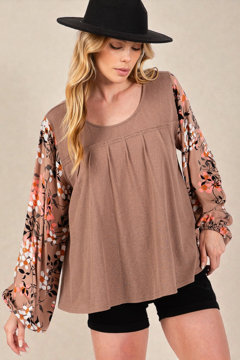 Woman wearing a brown top with floral sleeves and black shorts on a beige background