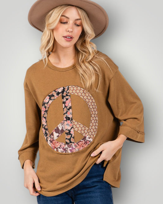 Woman wearing a brown sweatshirt with a floral peace symbol design on a plain background