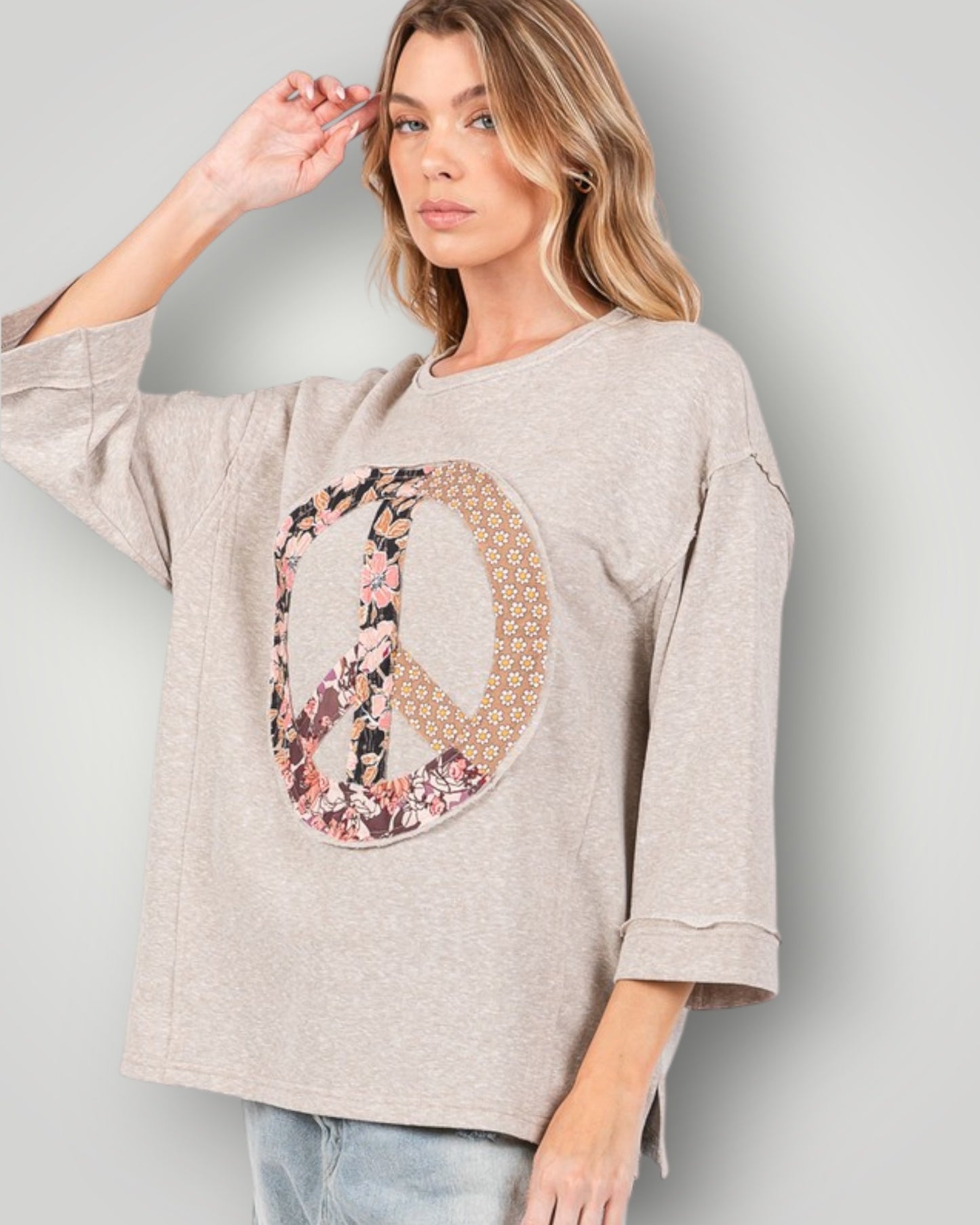 Woman wearing a beige sweater with a floral 'PEACE' design on a plain background