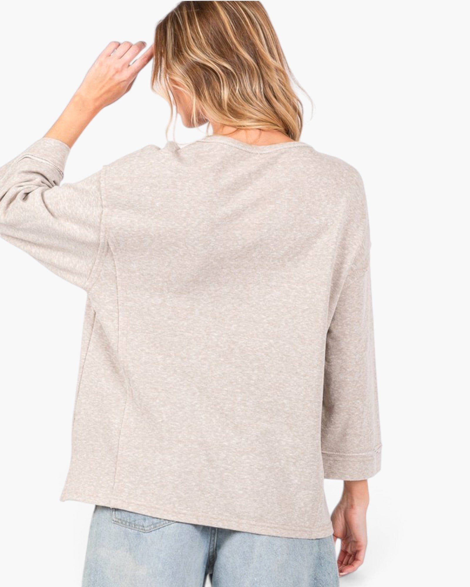 A woman shown from the back wearing a light heather beige long-sleeve top and light blue jeans against a plain white background.