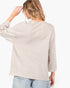 A woman shown from the back wearing a light heather beige long-sleeve top and light blue jeans against a plain white background.
