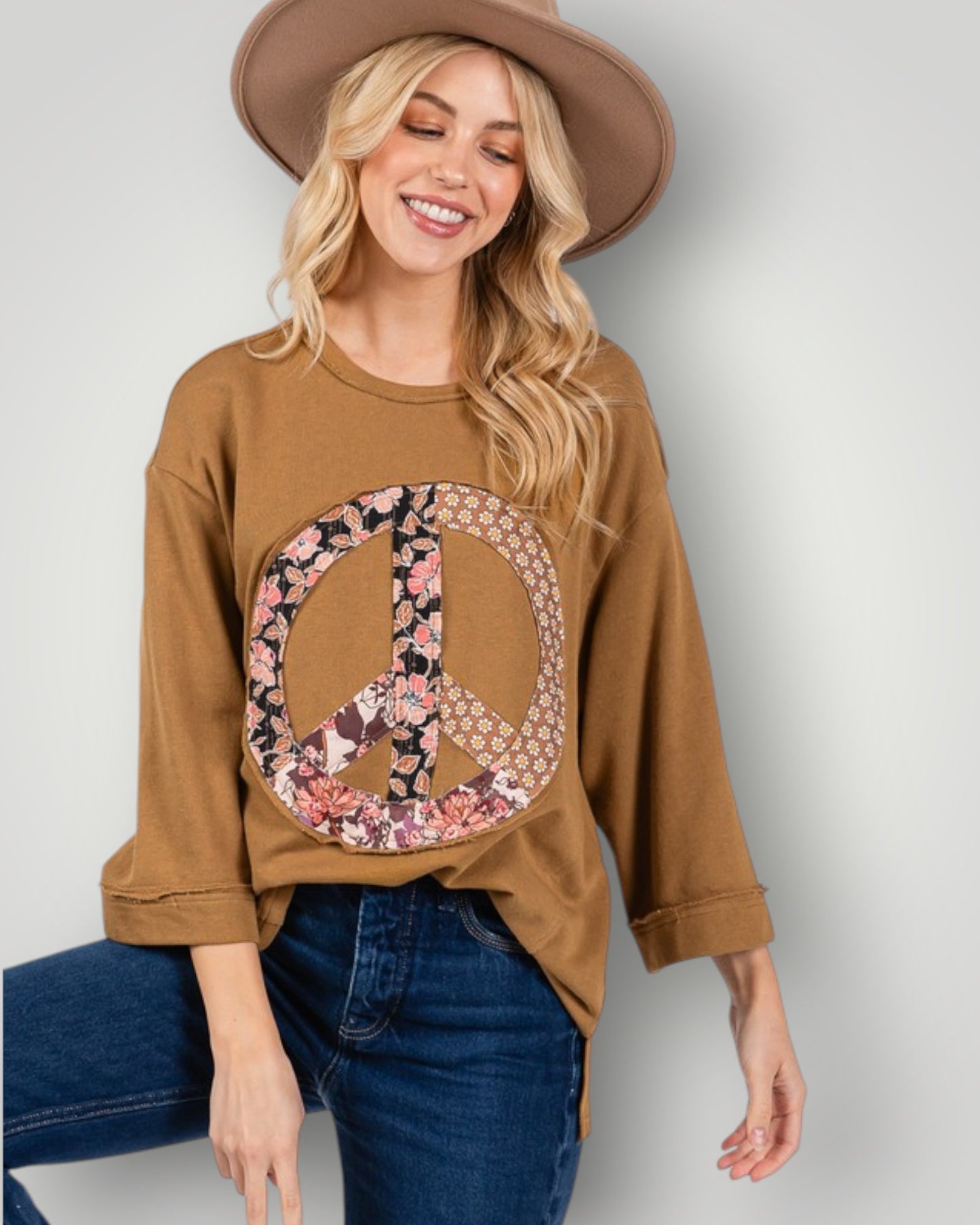 Woman wearing a brown sweatshirt with a peace symbol design, sitting against a plain background.