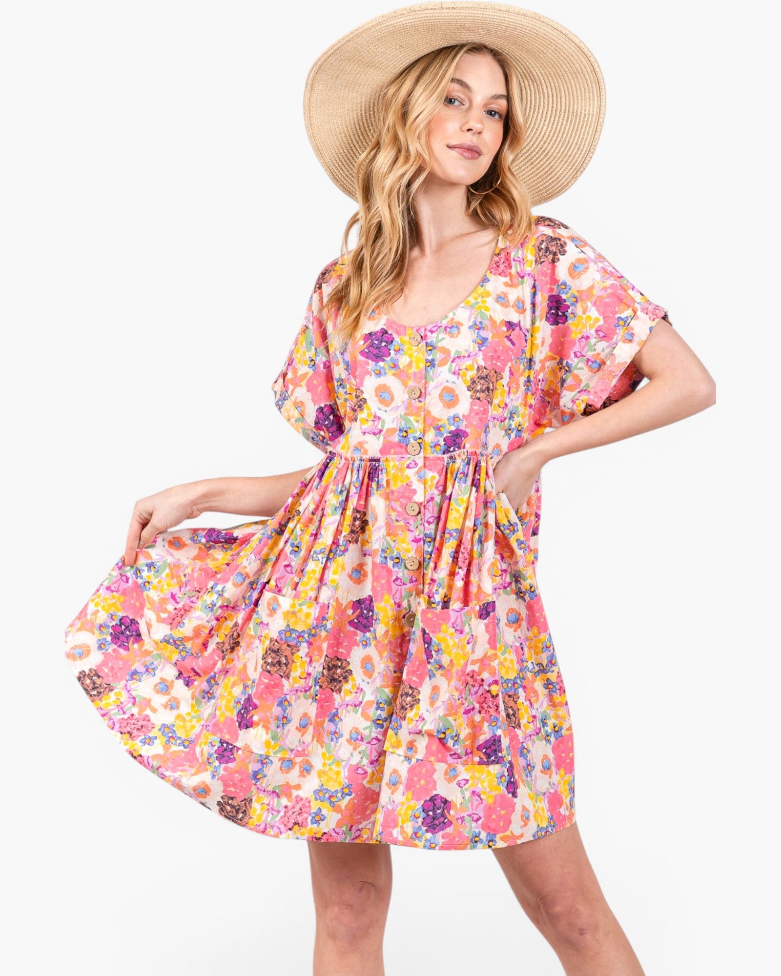 A woman wearing a short-sleeve, knee-length floral dress with a gathered waist and a wide-brim straw hat, posed against a plain white studio background.
