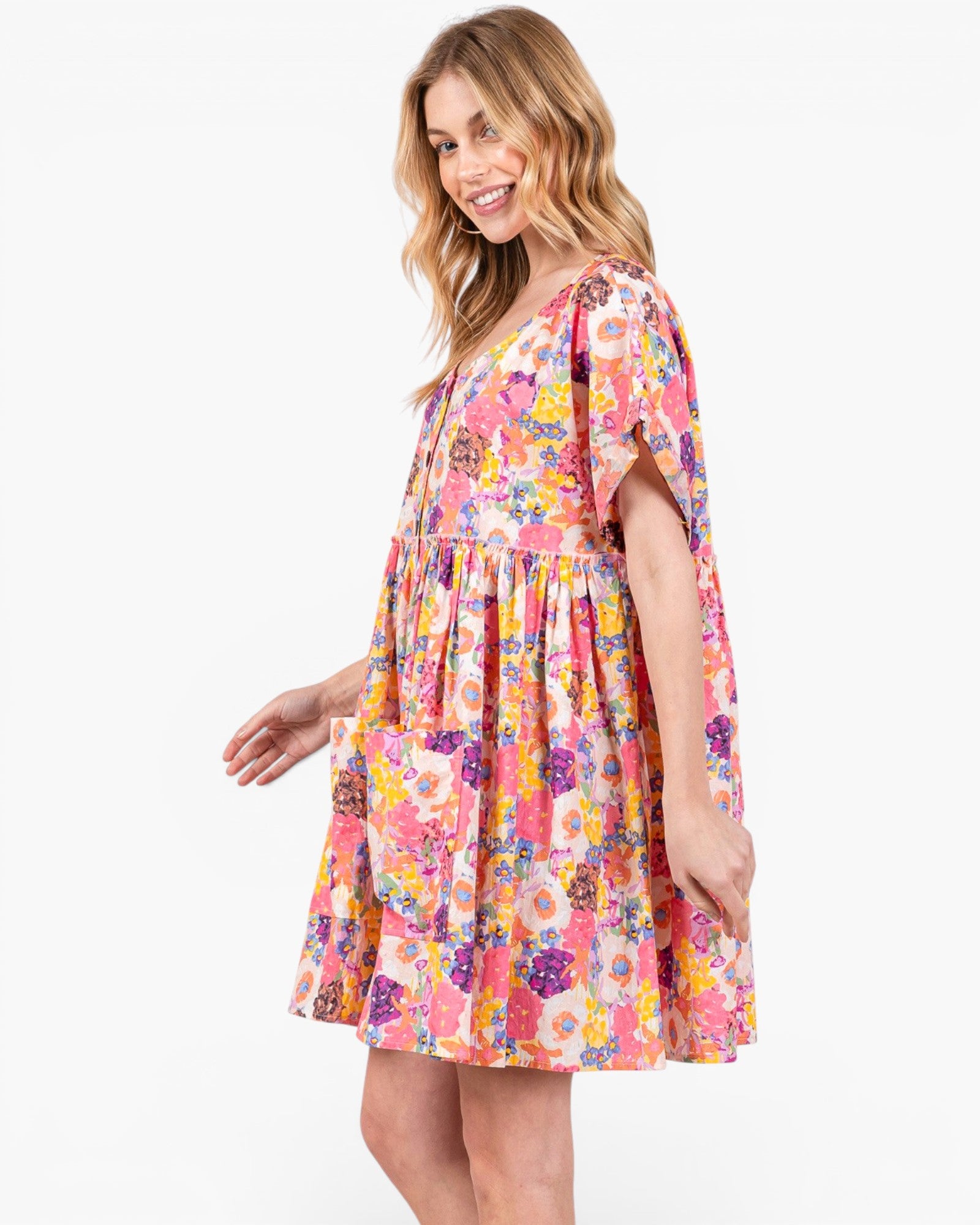 A woman modeling a short-sleeve tiered dress with a vibrant multicolor floral print on a solid white background.