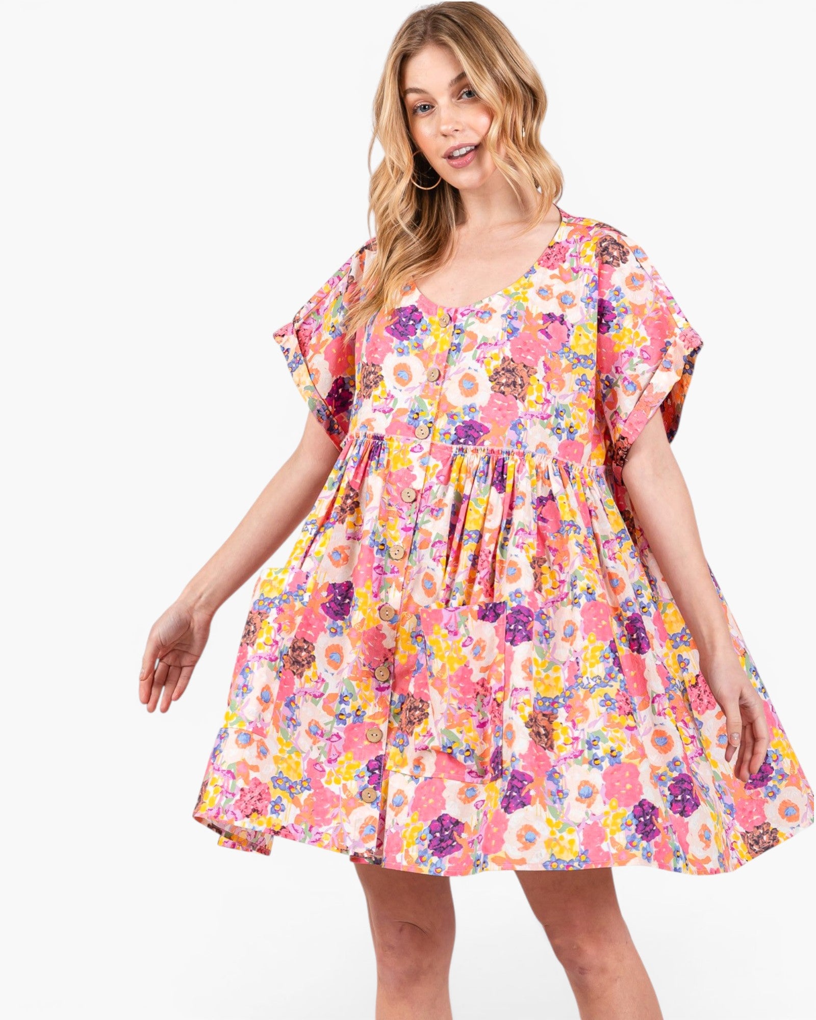 A woman modeling a short-sleeve tiered dress with a vibrant multicolor floral print on a light pink background, set against a plain white studio background.