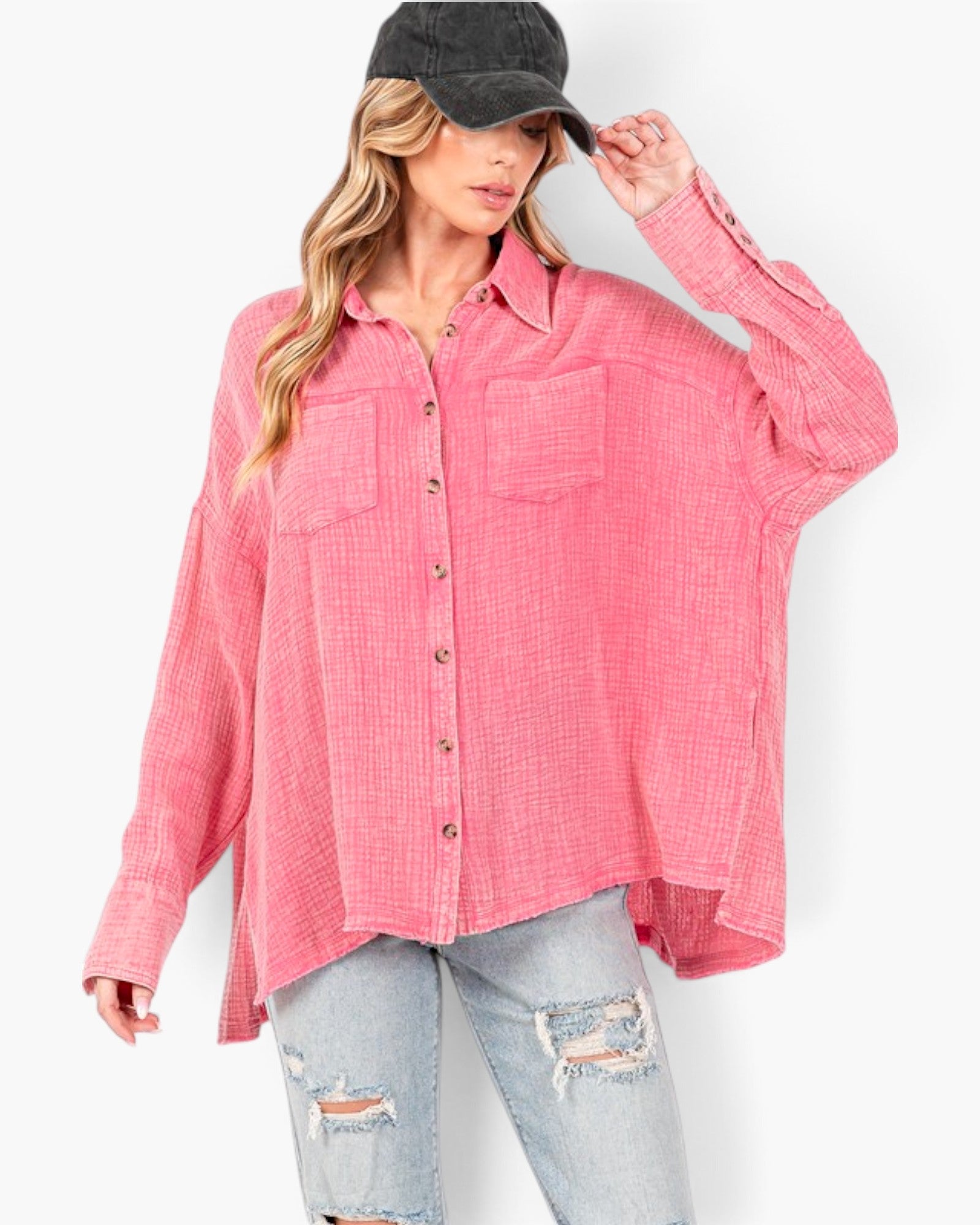 A woman wearing a pink textured button-up shirt with two chest pockets, styled with light-wash distressed jeans and a black baseball cap, against a plain white background.