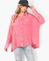 A woman wearing a pink textured button-up shirt with two chest pockets, styled with light-wash distressed jeans and a black baseball cap, against a plain white background.