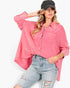 A woman wearing a pink textured button-up shirt with light-wash distressed jeans and a black baseball cap, posed against a plain white studio background.