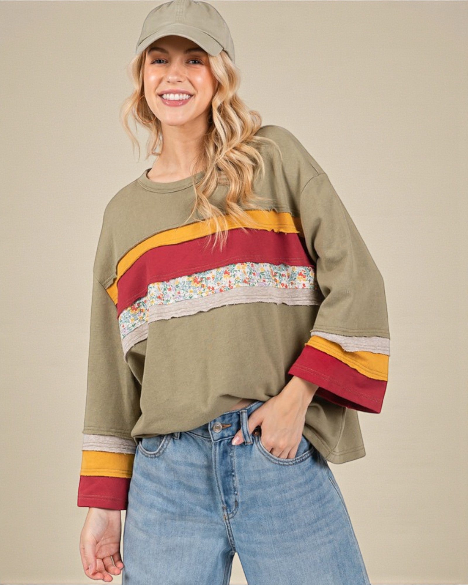 Woman wearing a green sweater with colorful stripes and floral pattern, paired with blue jeans and a beige cap.