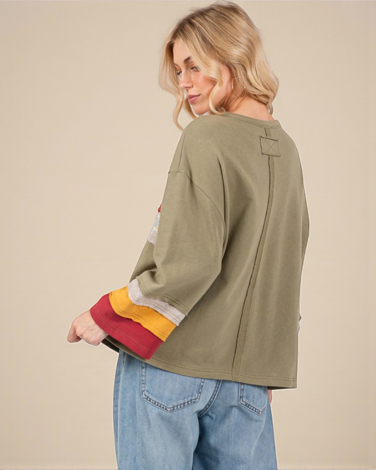 Woman wearing an olive green long-sleeve shirt with colorful cuffs and jeans on a beige background