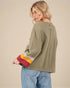 Woman wearing an olive green long-sleeve shirt with colorful cuffs and jeans on a beige background