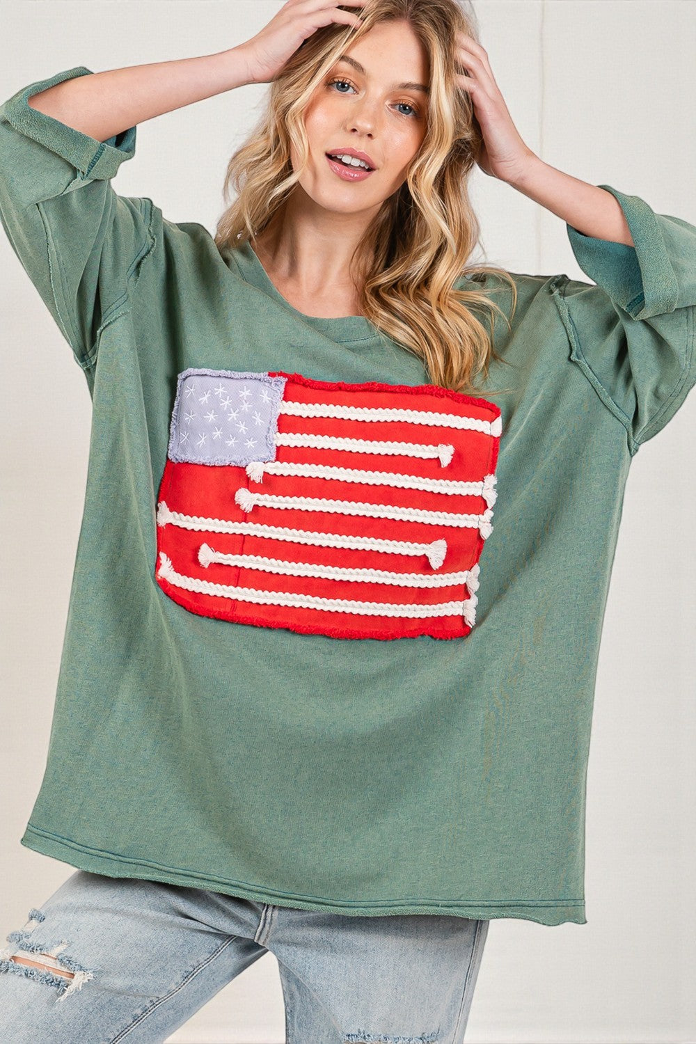 Woman wearing a green sweatshirt with an American flag patch on a plain background