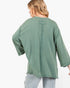 A woman shown from the back wearing an oversized sage green top with a vertical seam and tie detail at the neckline, paired with light wash jeans against a plain white background.