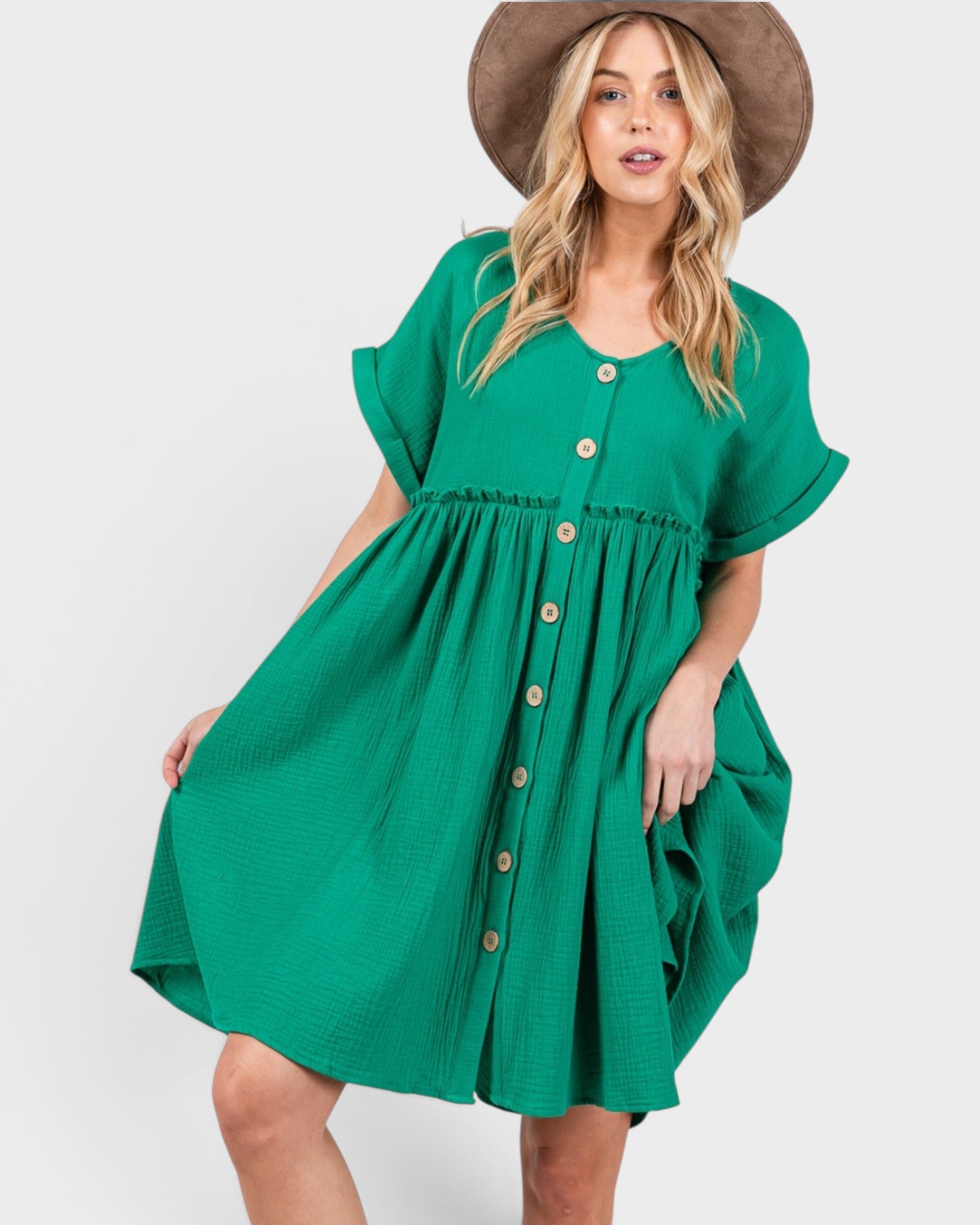 A woman wearing a bright green short-sleeve button-front dress with a gathered waist and a brown wide-brim hat, photographed against a light gray studio background.