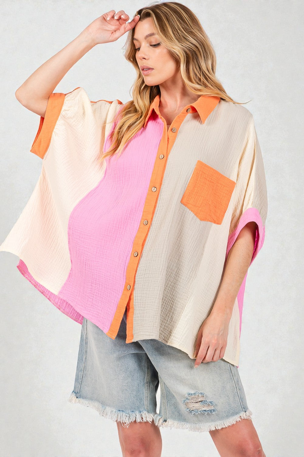 Woman wearing a colorful cardigan over a pink shirt with denim shorts on a white background