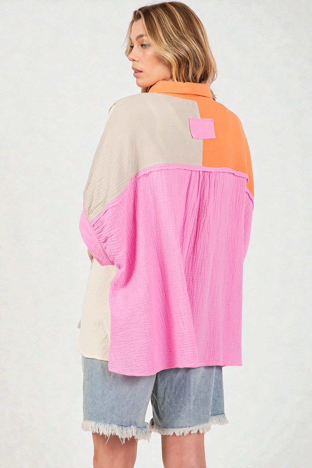 Person wearing a colorful jacket with pink, orange, and beige sections on a white background