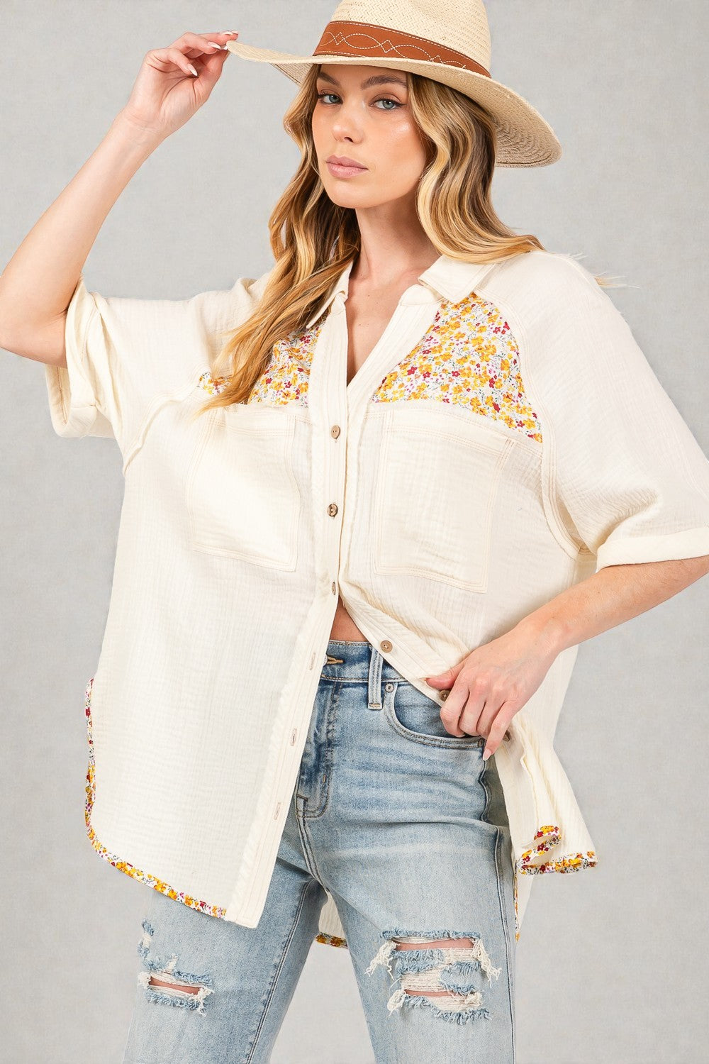 Woman wearing a cream-colored blouse with floral embroidery and denim jeans on a gray background