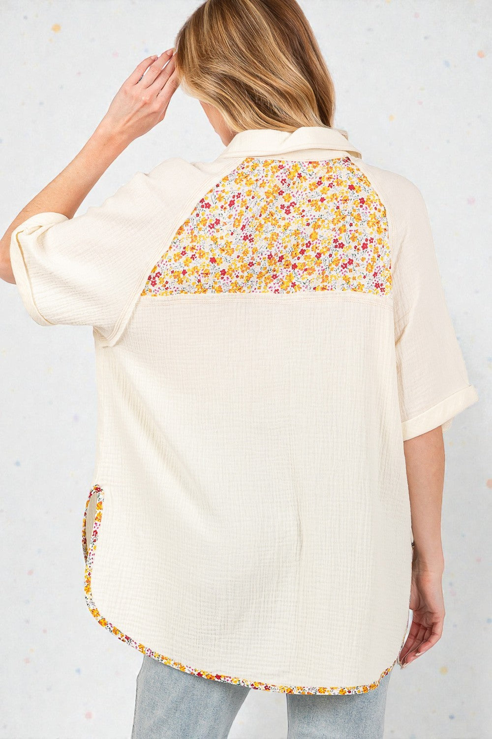 Woman wearing a cream-colored shirt with a floral pattern on the back, standing against a light background.