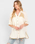 A woman wearing a cream-colored short-sleeve button-up shirt with yellow and white floral embroidery on the chest, paired with distressed light blue jeans, against a light gray studio background.