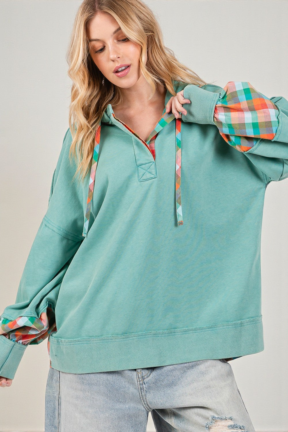 Woman wearing a teal pullover with plaid sleeves against a plain background