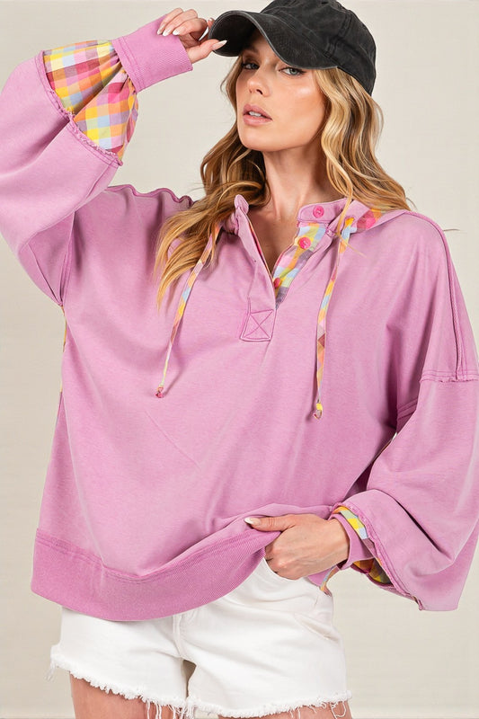 Woman wearing a pink pullover with colorful accents and a black cap.