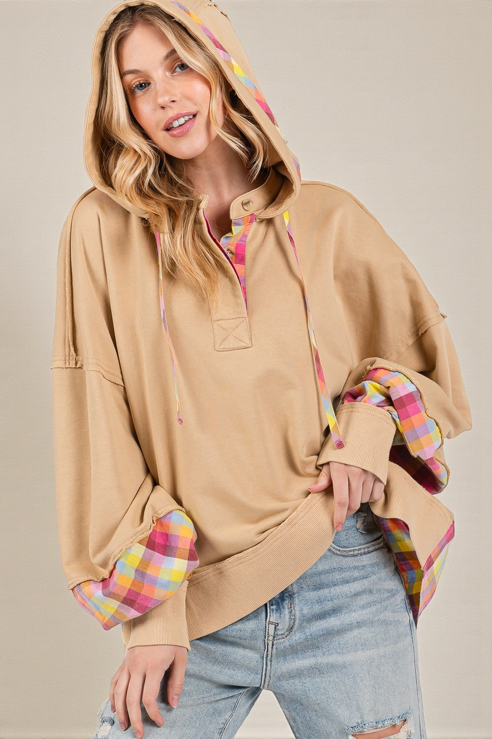 Woman wearing a beige hoodie with colorful cuffs and hem on a plain background