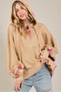 Woman wearing a beige hoodie with colorful cuffs and hem on a plain background