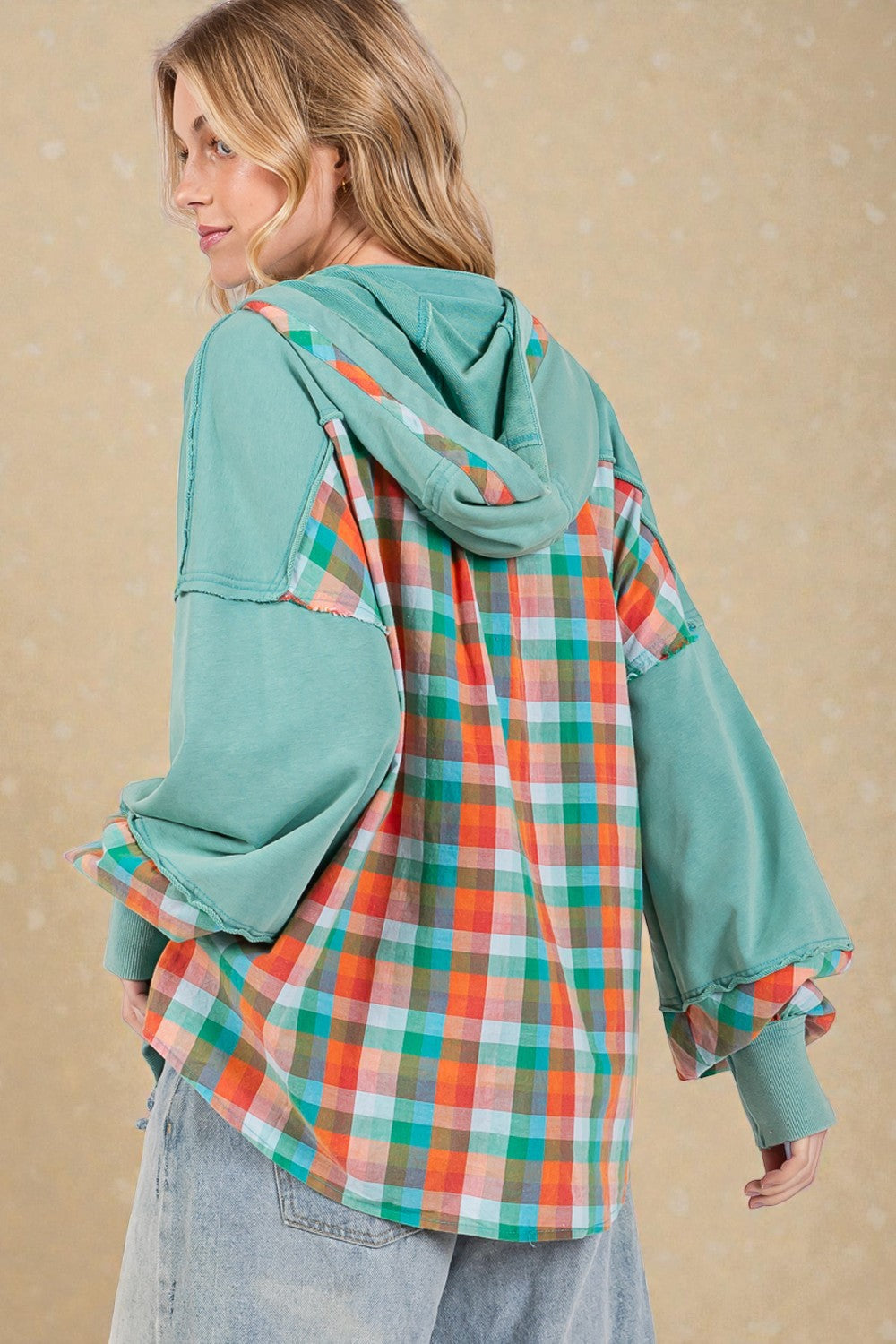 Person wearing a teal hoodie over a plaid shirt against a beige background