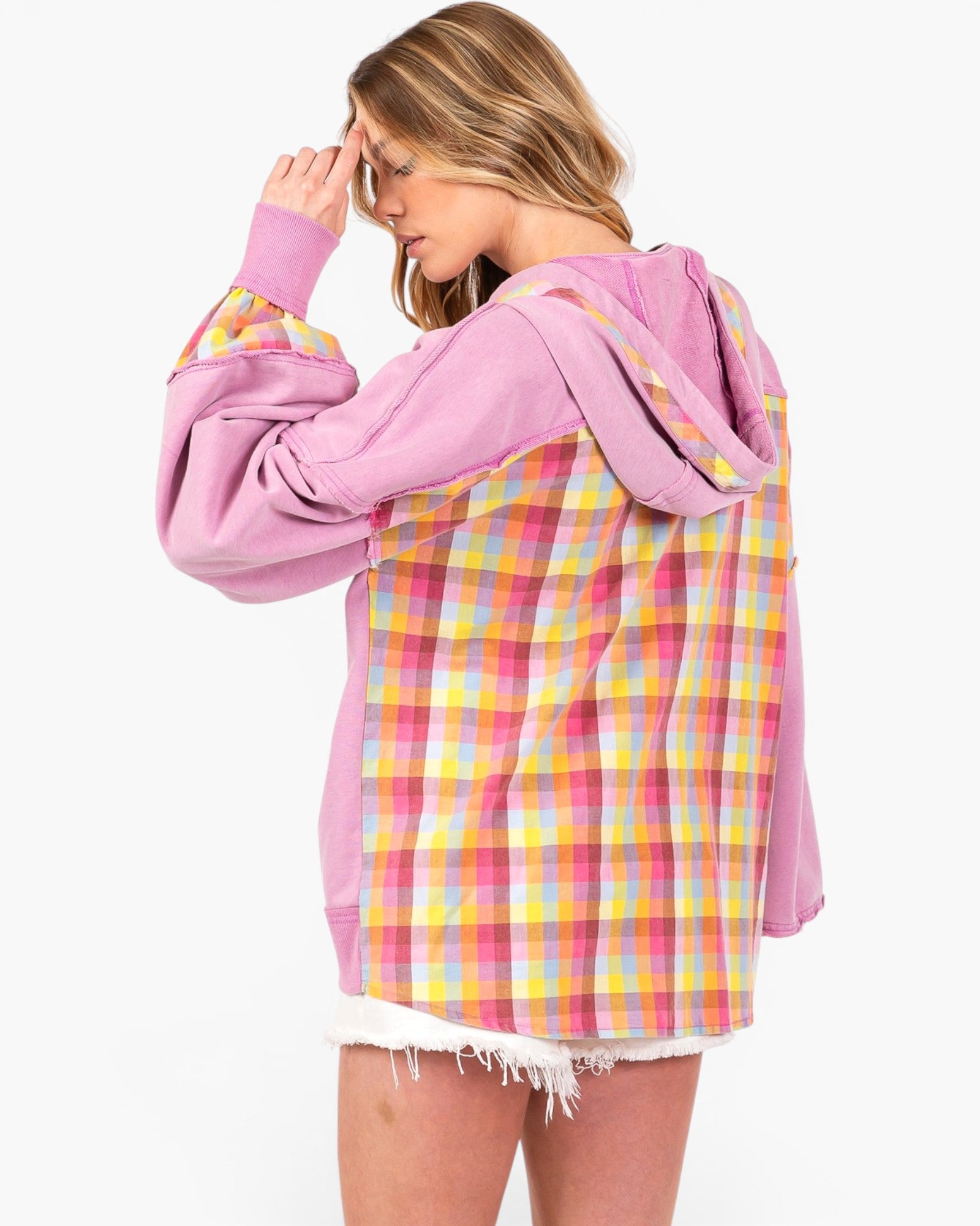 A woman wearing an oversized hoodie with a pink base and a yellow, pink, and white plaid pattern on the back and sleeves, shown from a side-back angle against a plain white background.
