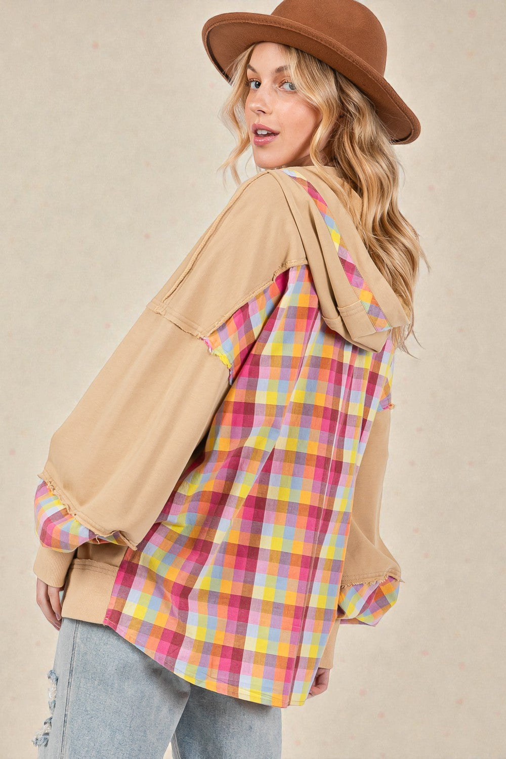 Woman wearing a plaid shirt with a beige jacket and brown hat on a beige background