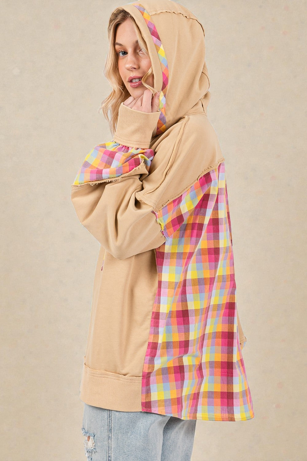 Person wearing a beige hoodie with a colorful plaid pattern underneath on a beige background