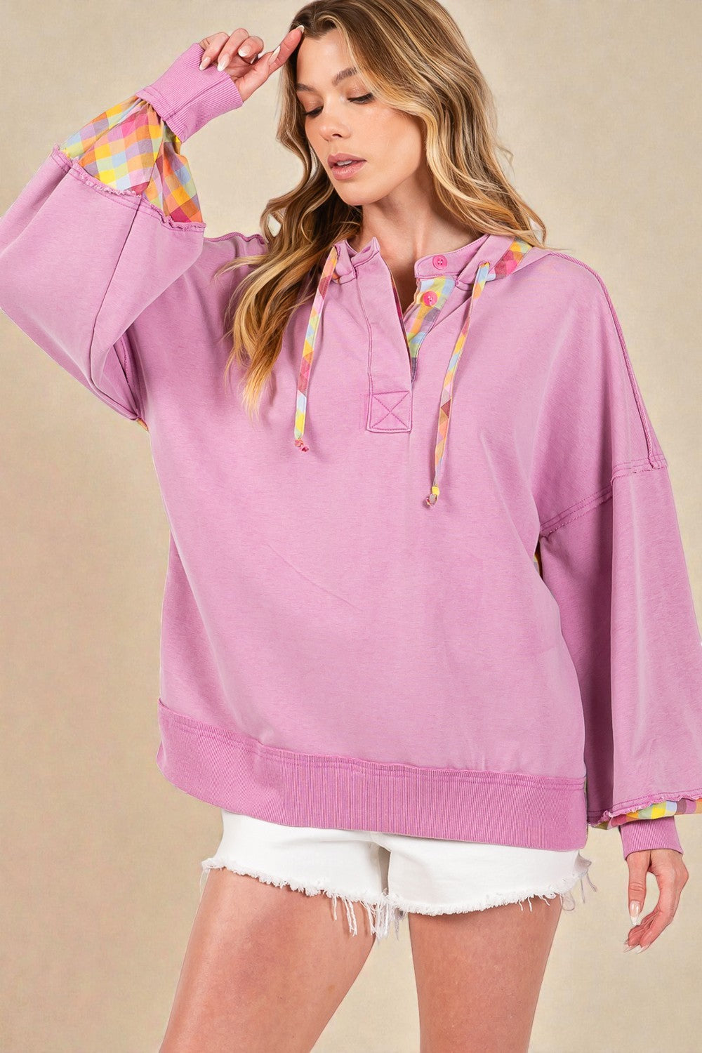 Woman wearing a pink hoodie with colorful sleeves against a beige background