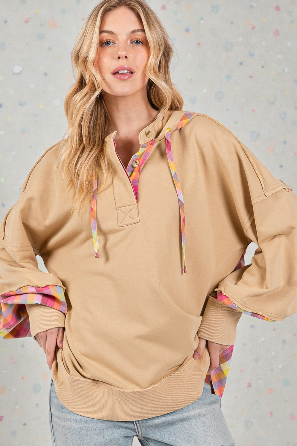 Woman wearing a beige hoodie with colorful accents against a light gray background